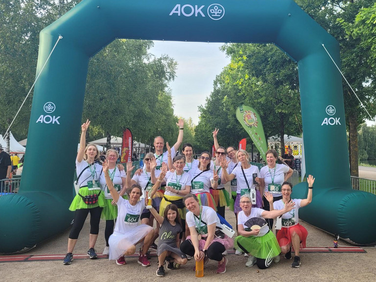 Mitarbeitende aus Pflege, Koordination/Verwaltung, Ehrenamt und Geschäftsführung des Albertinen Hospiz Norderstedt beim AOK-Firmenlauf Norderstedt 2026 blicken gemeinsam im Zieleinlauf ausgelassen und glücklick in die Kamera. Mitarbeitende aus Pflege, Koordination/Verwaltung, Ehrenamt und Geschäftsführung des Albertinen Hospiz Norderstedt beim AOK-Firmenlauf Norderstedt 2026 blicken gemeinsam im Zieleinlauf ausgelassen und glücklick in die Kamera.